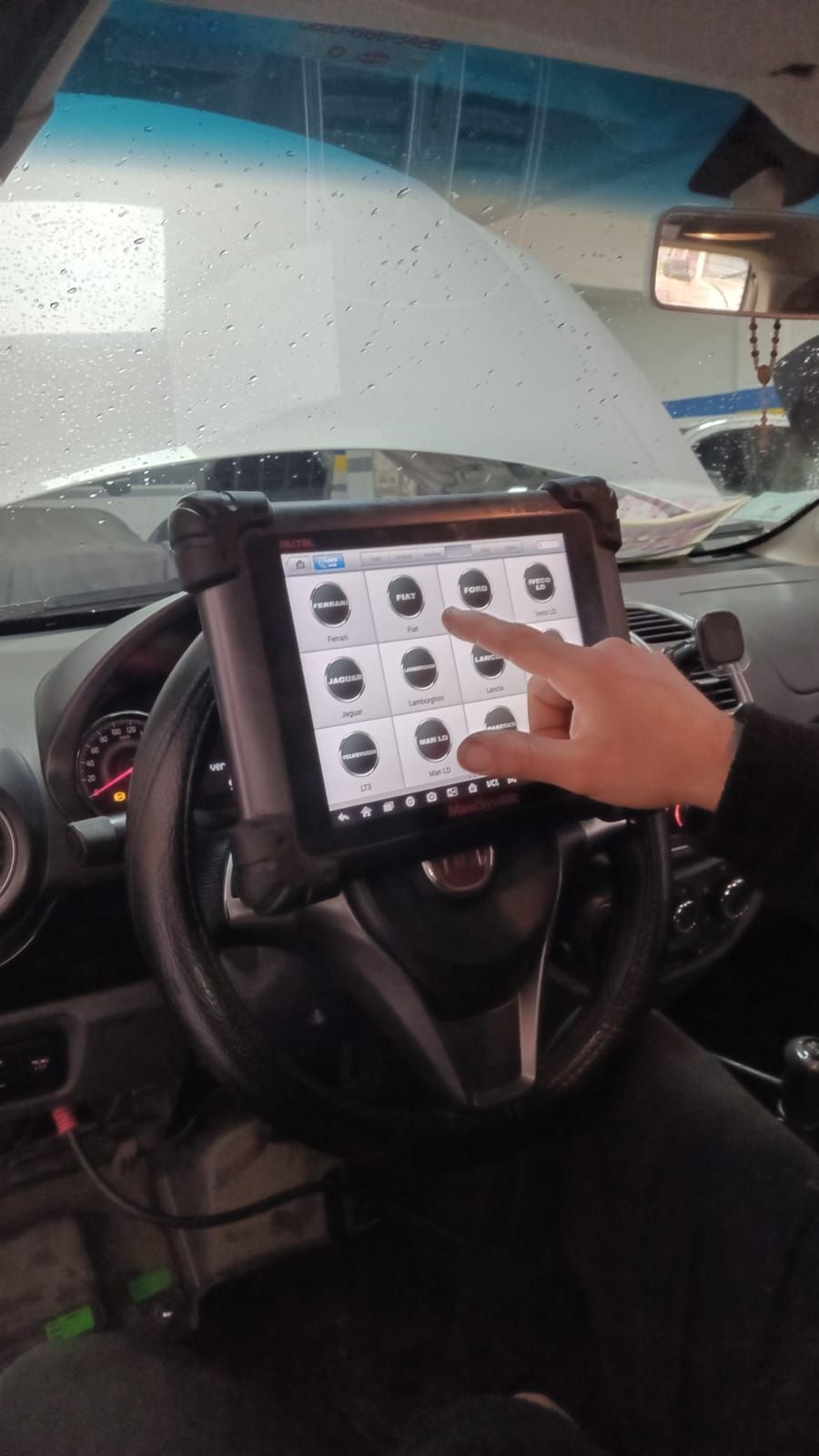 Mecánico diagnosticando un coche plateado con un ordenador portátil en un taller.
