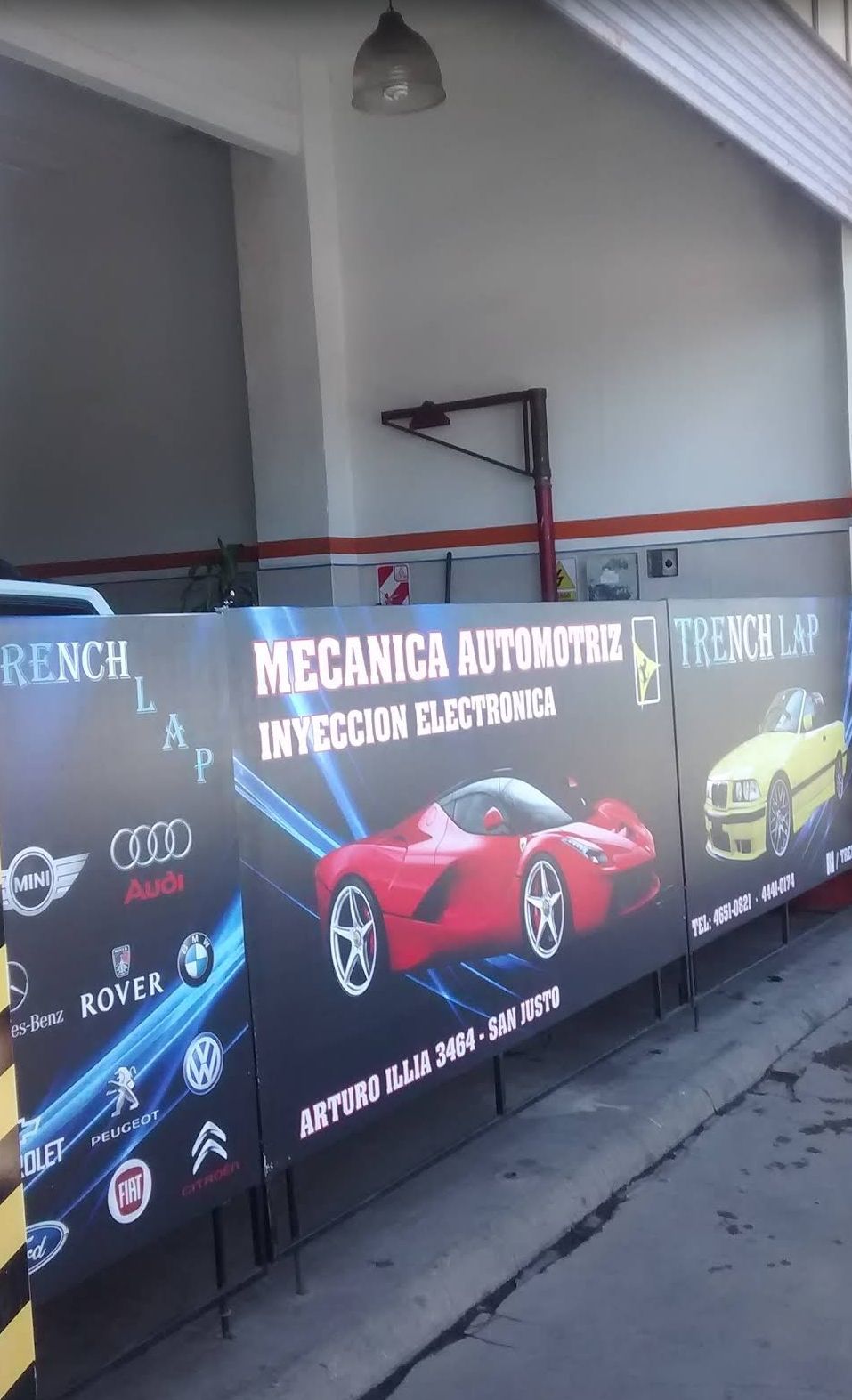 Interior de taller de carrocería con un SUV negro en un elevador, herramientas y paredes blancas brillantes.
