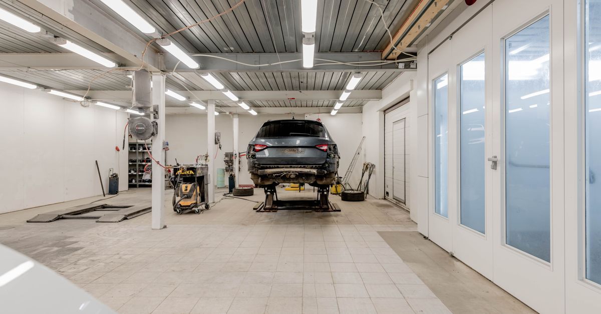 Interior de taller de carrocería con un SUV negro en un elevador, herramientas y paredes blancas brillantes.