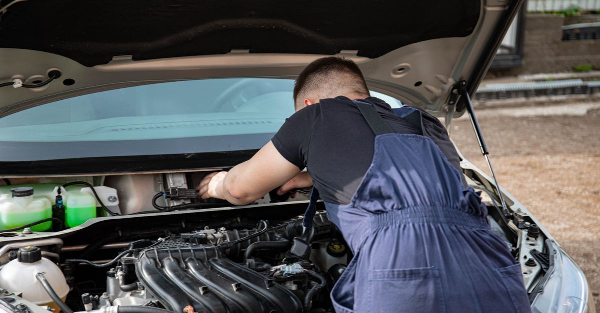 Persona inclinada hacia el compartimento del motor de un coche, con el capó abierto, inspeccionando o reparando el motor.