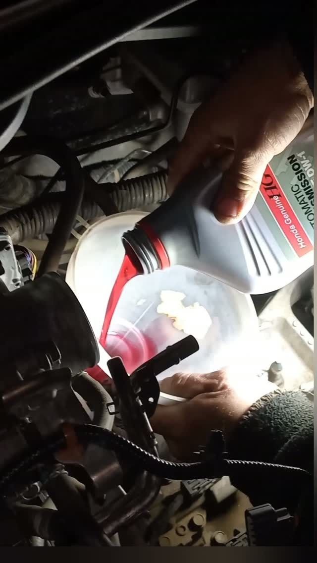 Verter manualmente aceite de motor de un recipiente al motor de un automóvil bajo la luz brillante de una linterna.