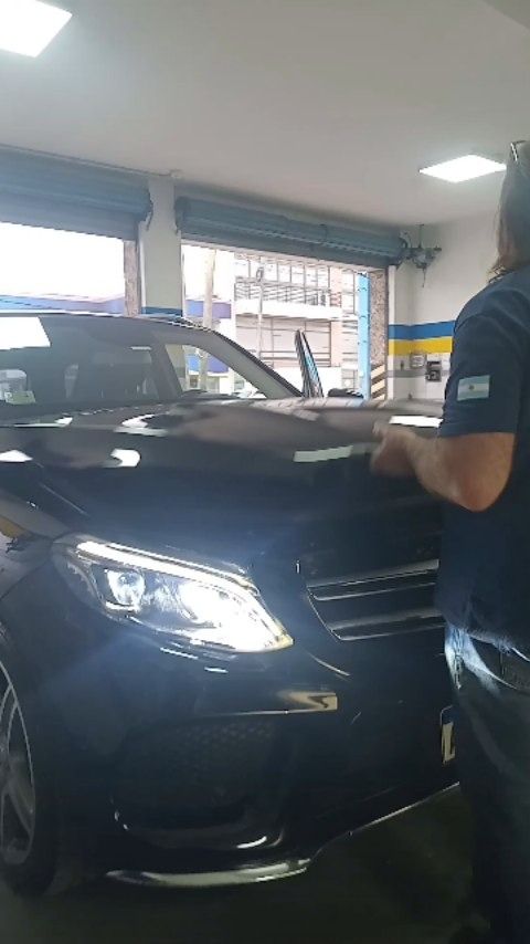 Mecánico inspeccionando un coche negro dentro de un taller mecánico bien iluminado.