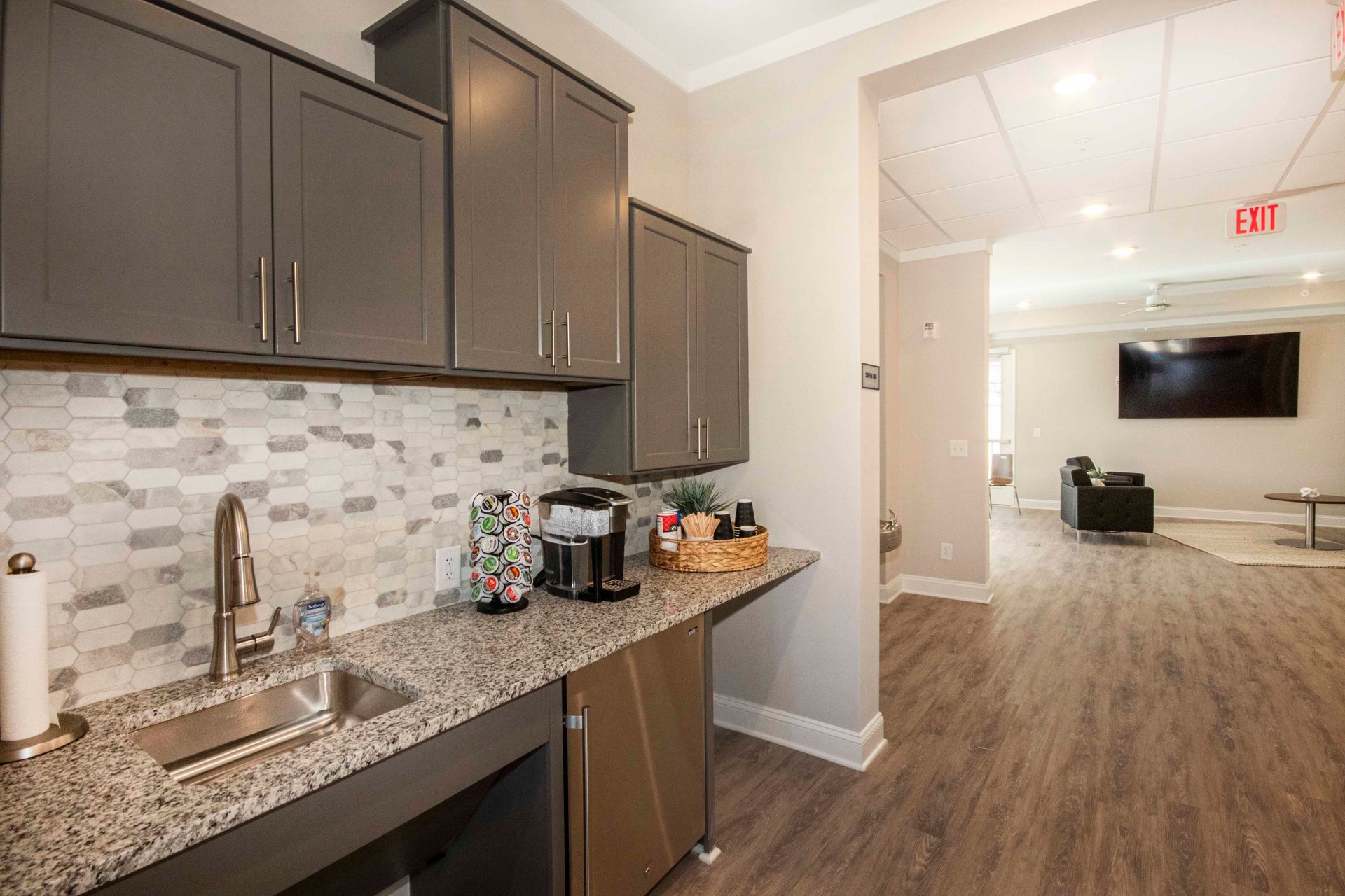 A kitchen with granite counter tops , gray cabinets , a sink and a dishwasher.