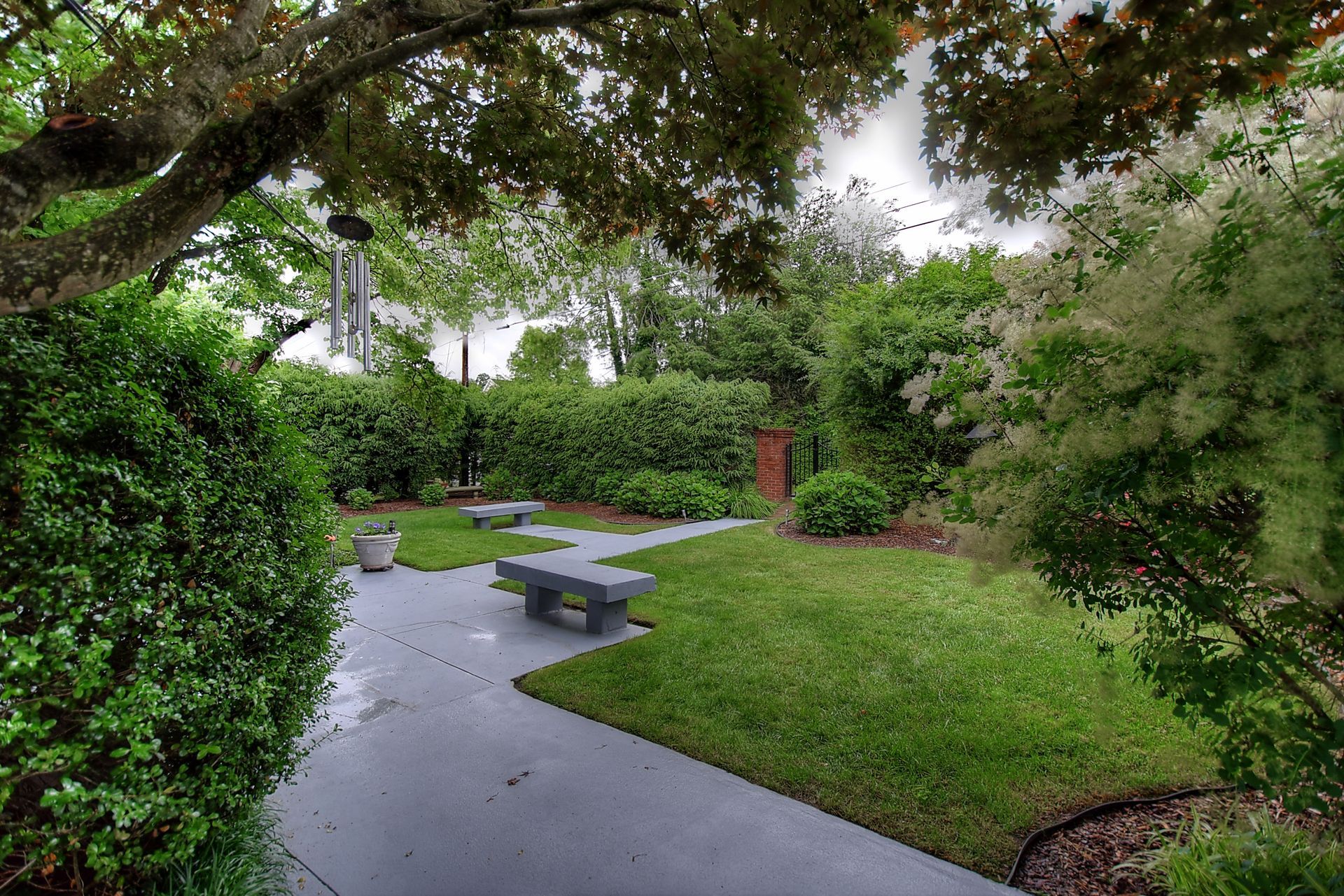 A lush green park with a path and benches surrounded by trees and bushes.