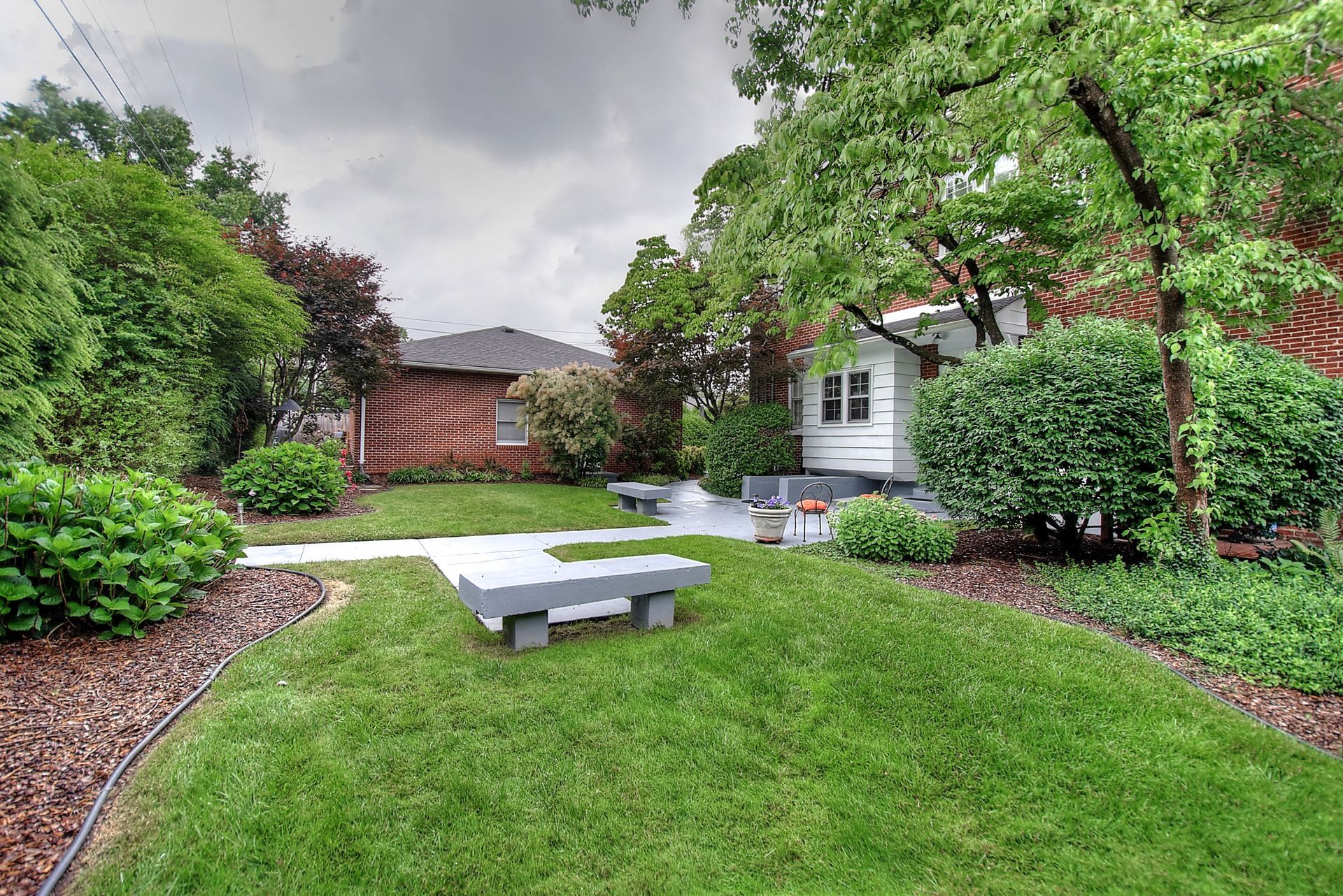 A lush green yard with a bench in the middle of it and a house in the background.