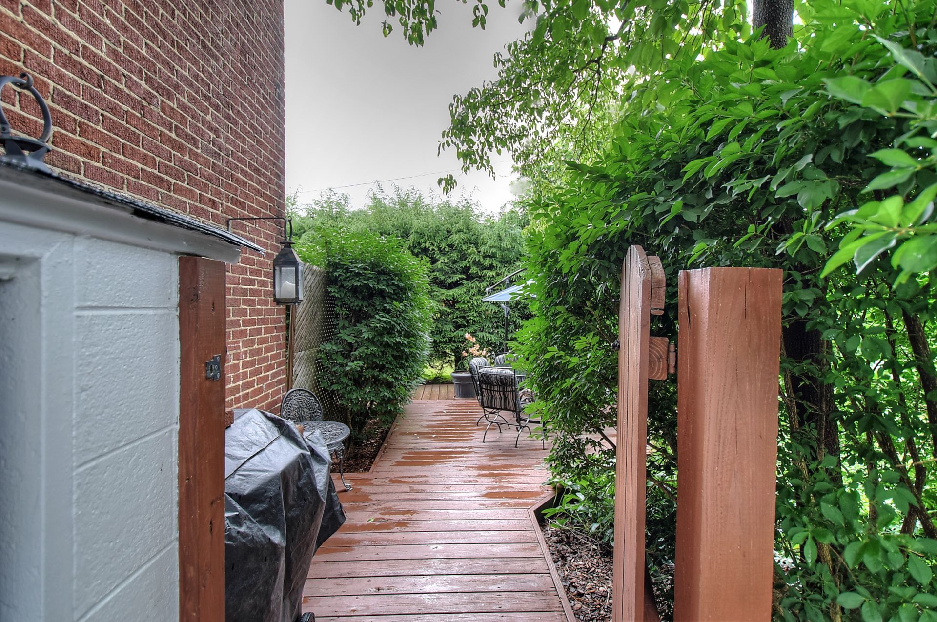 A wooden walkway leading to a brick building with a grill in the background.