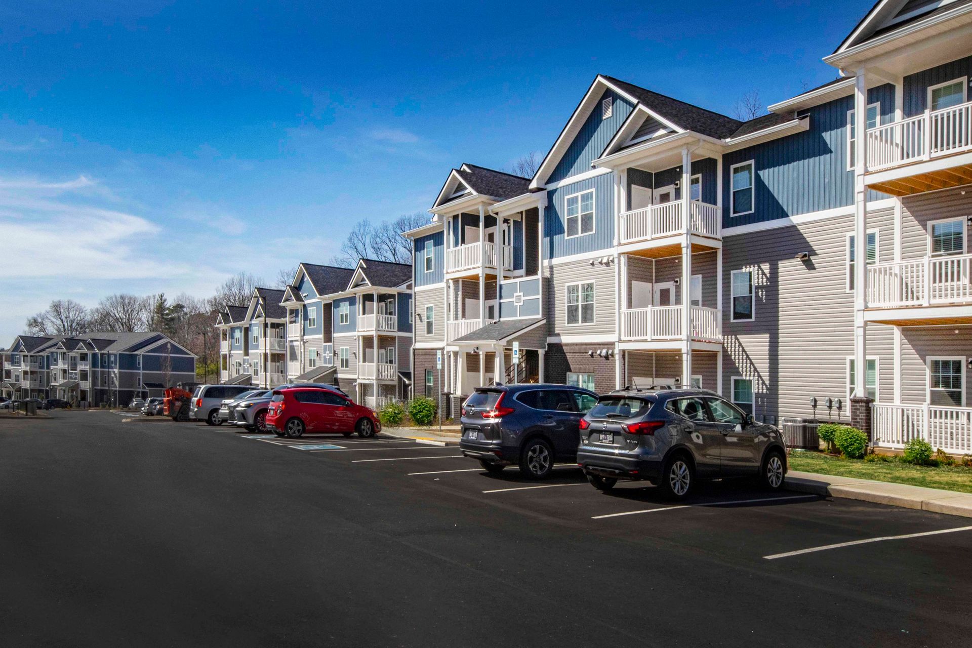A row of cars are parked in front of a large apartment building.