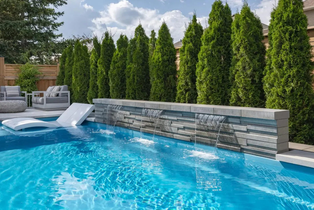 Une grande piscine avec une cascade dans l'arrière-cour entourée d'arbres.
