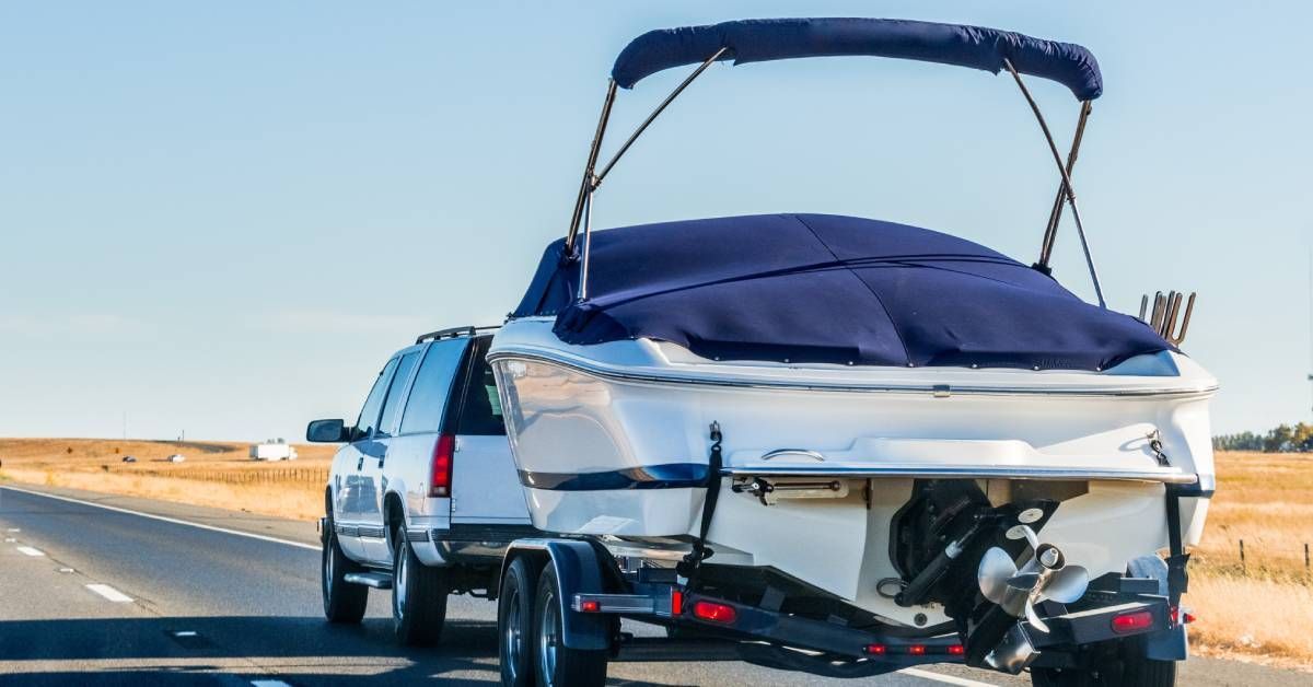 An image of a white SUV hauling a medium-sized white boat equipped with a cover while driving down the highway.