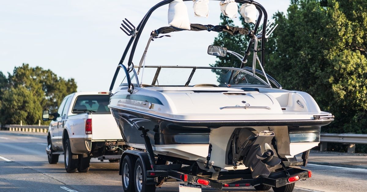 A white pickup truck driving along an interstate highway while hauling a white and black motorboat behind.
