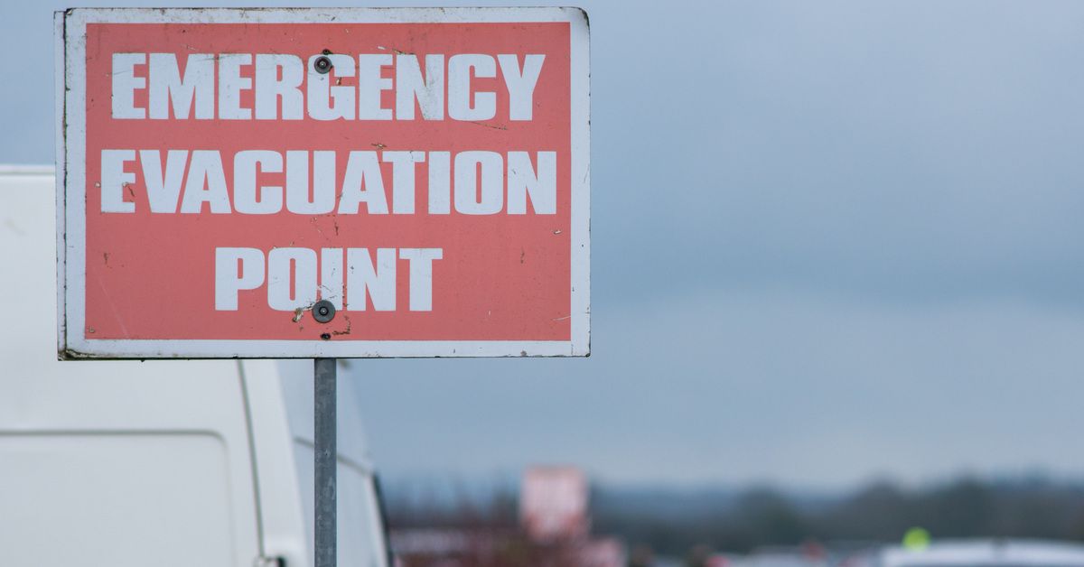 A red sign on the side of a highway that reads 'Emergency Evacuation Point.' Traffic is backed up in the background.