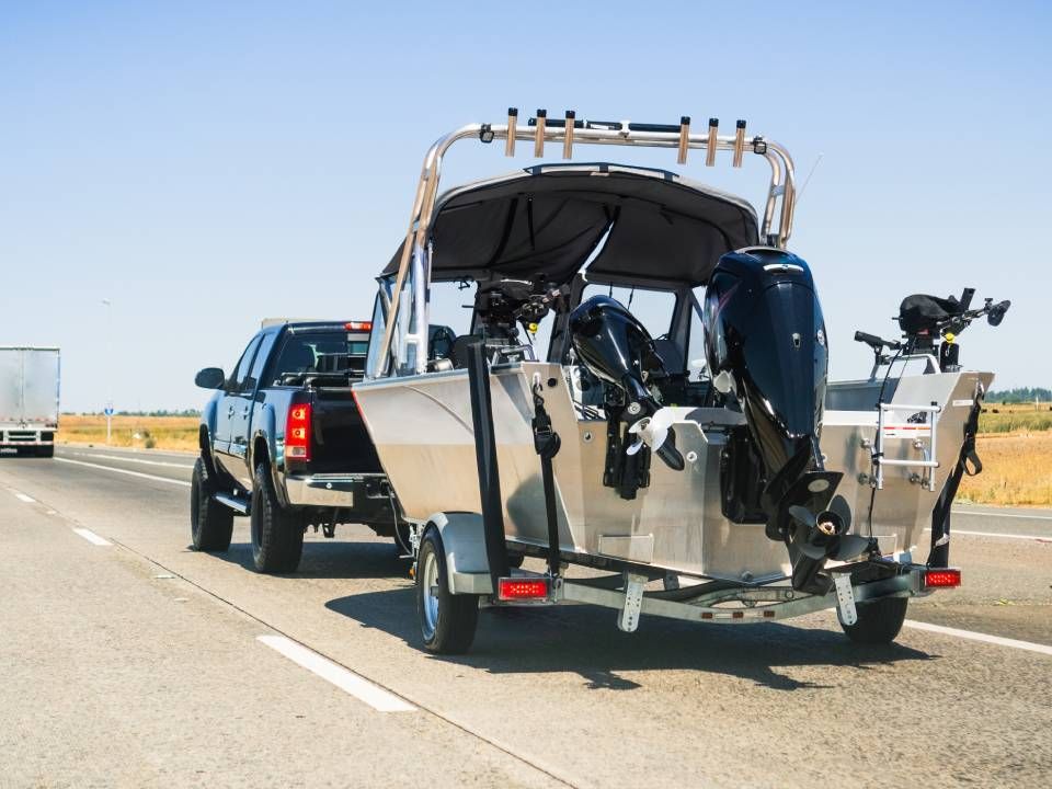 A black pickup truck towing a chrome-colored motor boat with a black propeller behind it on a highway