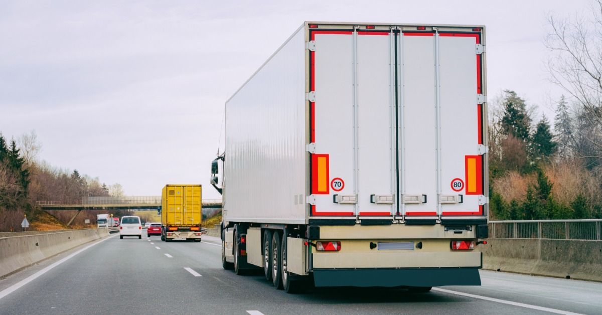 A white semi truck drives down a two-lane highway. Several other cars and semi trucks drive ahead on the road.