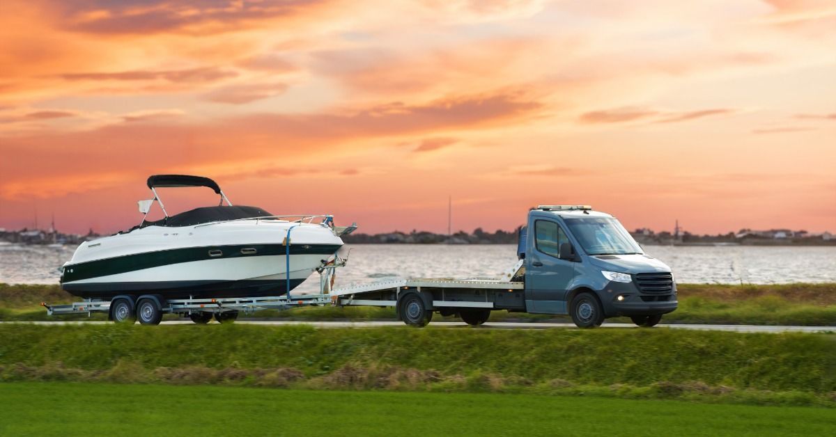 A black and white boat is strapped to a trailer and being driven by a truck. The sun sets behind the boat.