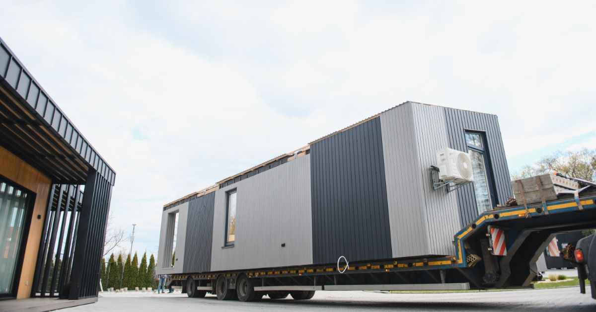 A manufactured tiny home with light grey and dark grey siding resting on a flatbed trailer.