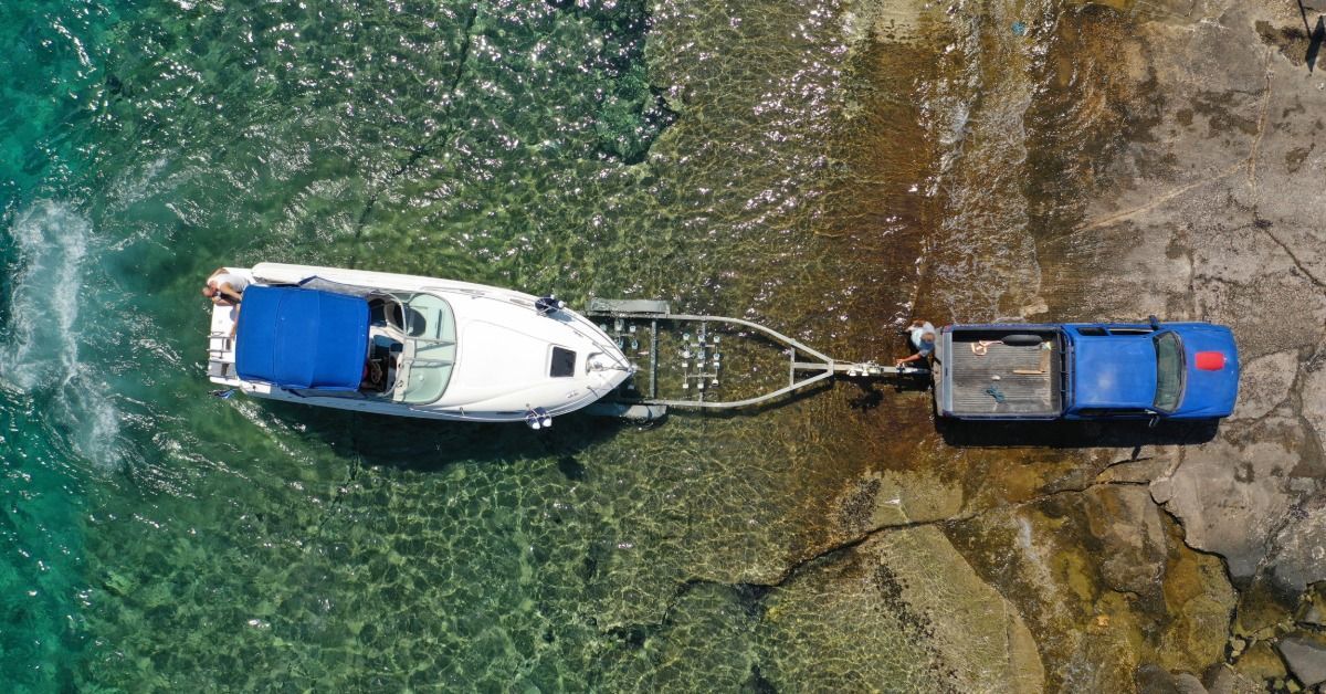 A white speedboat rests on a trailer pulled from turquoise water. A truck pulls the trailer from the shoreline.