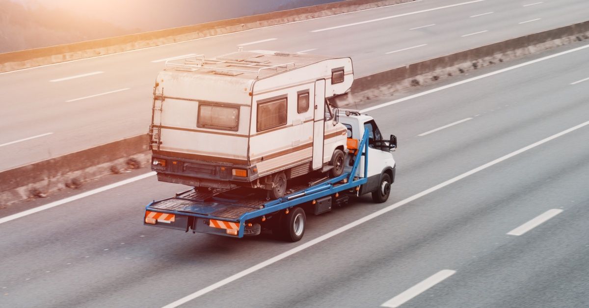A truck hauling a white vintage camper along a highway with a mountain view. The sun is rising behind the mountain.