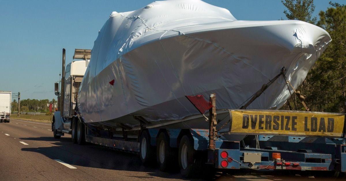 A wrapped boat travels on a transport trailer along a highway as an oversize load