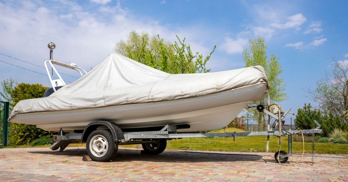 A covered boat rests on a trailer at a residential property while awaiting pickup for transportation.