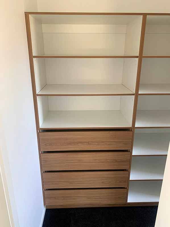 A walk in closet with wooden shelves and drawers.