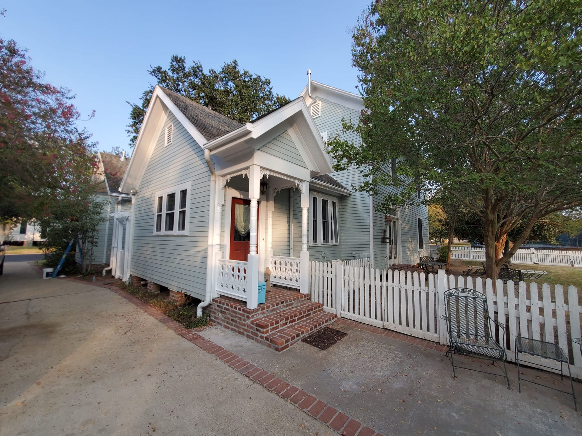 White cottage with porch and picket fence along a tree-lined street at dusk
