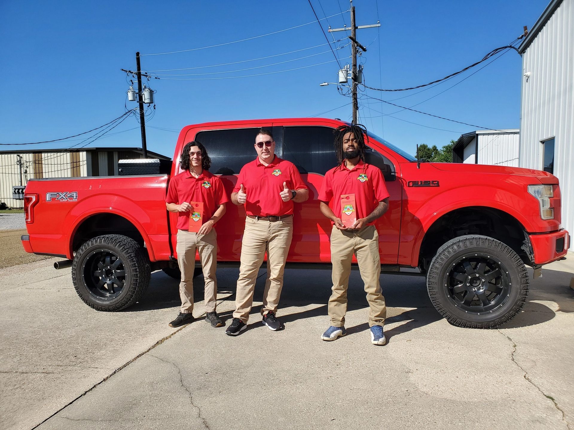 Three people standing in front of a red pickup truck on a sunny street