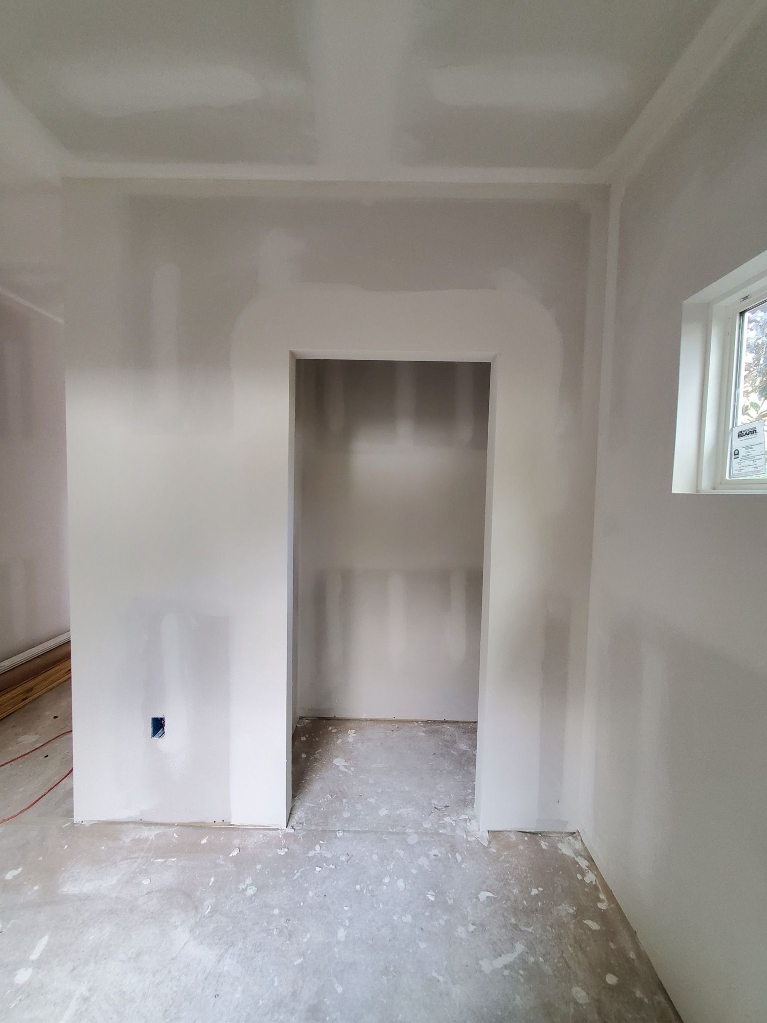 Empty white room under renovation with exposed floor, open closet, and a small window