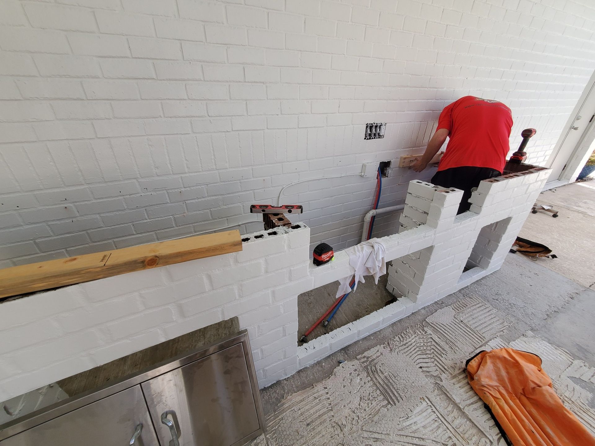 Worker in red shirt installing a white wall panel in an indoor construction area