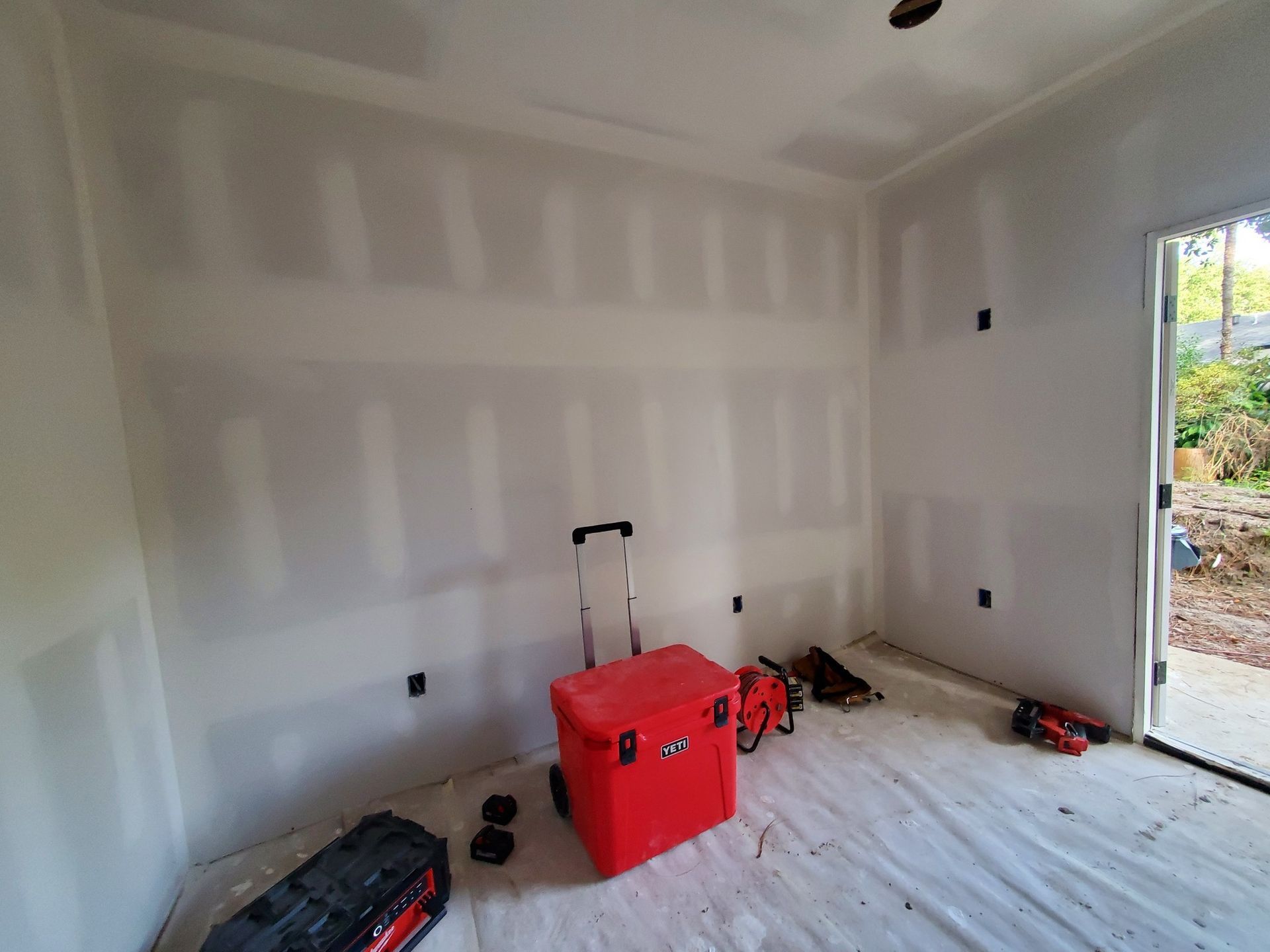 Unfinished drywall room with a red toolbox and scattered tools on the floor near an open doorway.