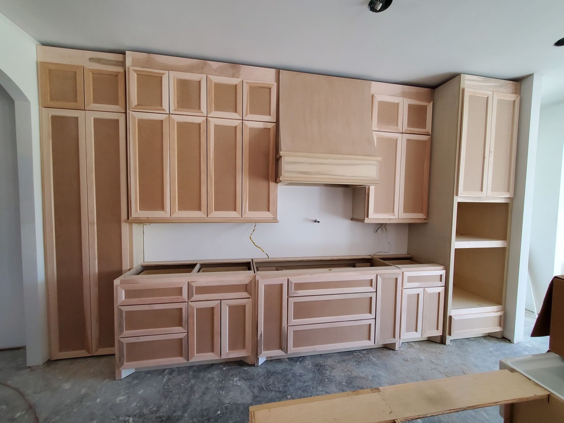 Unfinished kitchen cabinets and countertops installed against a wall, with beige wood frames and a bare floor.