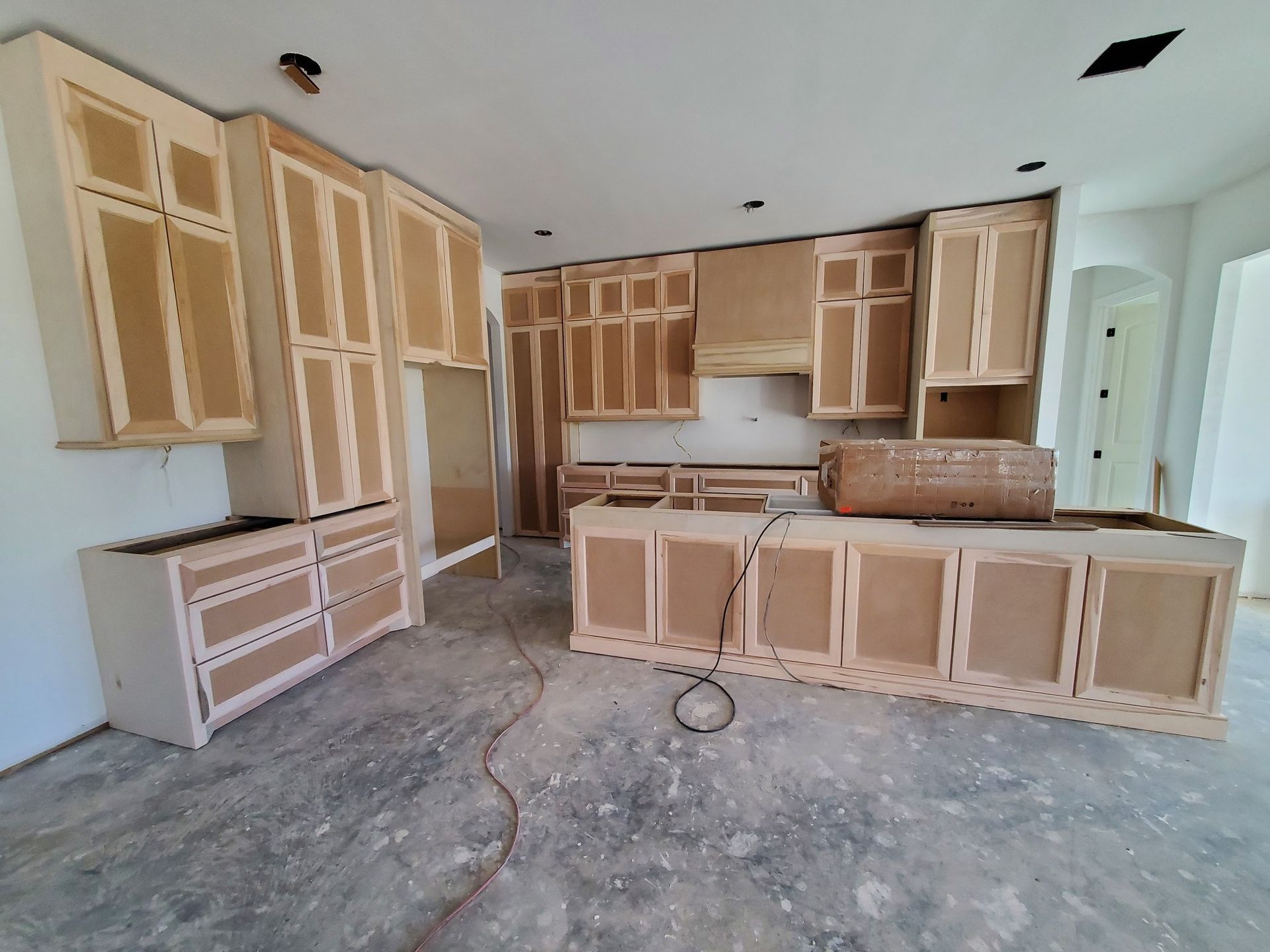 Unfinished kitchen with bare plywood cabinets and island on a concrete floor under construction
