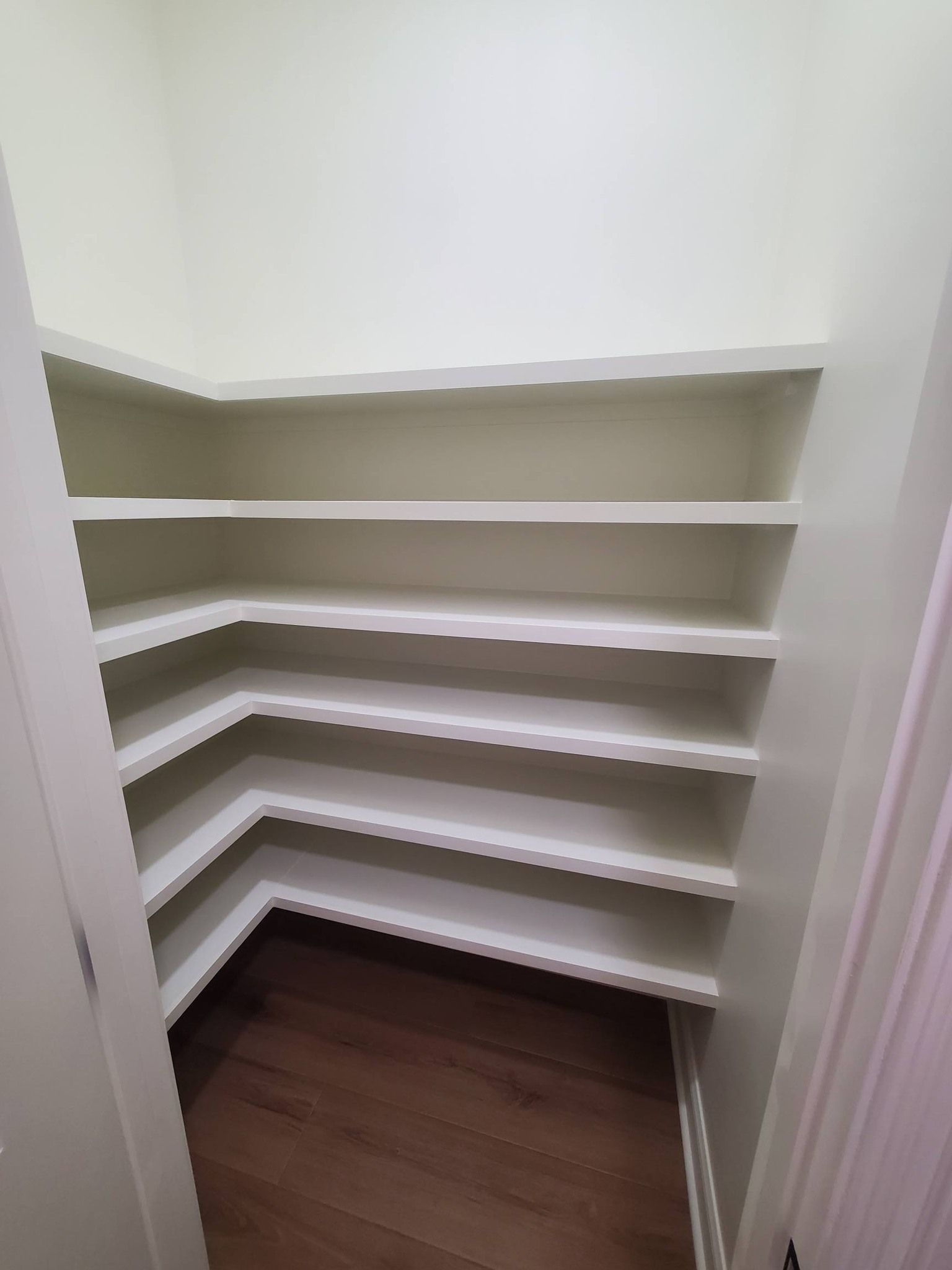 Walk-in closet with white shelves and dark wood floor, viewed from the doorway
