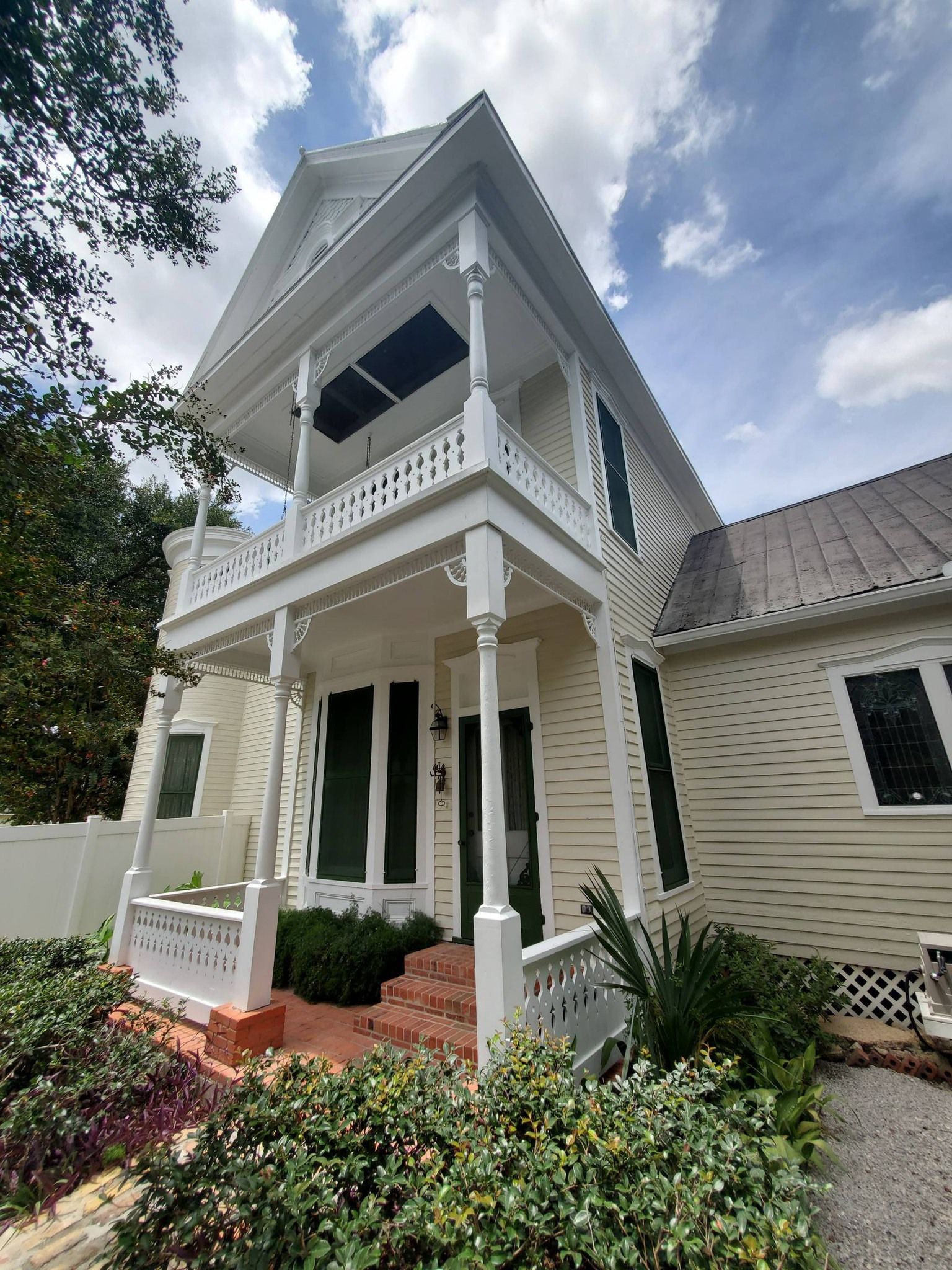 Victorian-style house with a white porch, blue awning, brick steps, and landscaped front yard