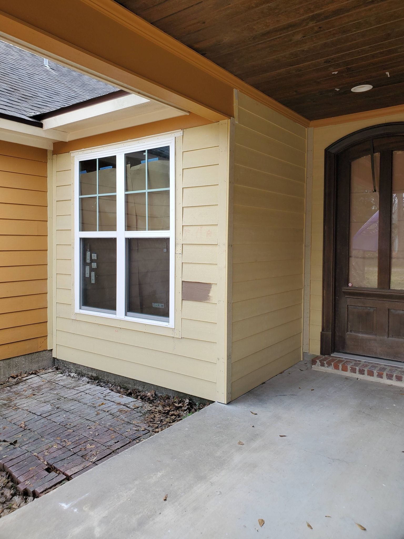 Covered front entry with cream siding, white-framed window, and a dark wooden door on a concrete porch
