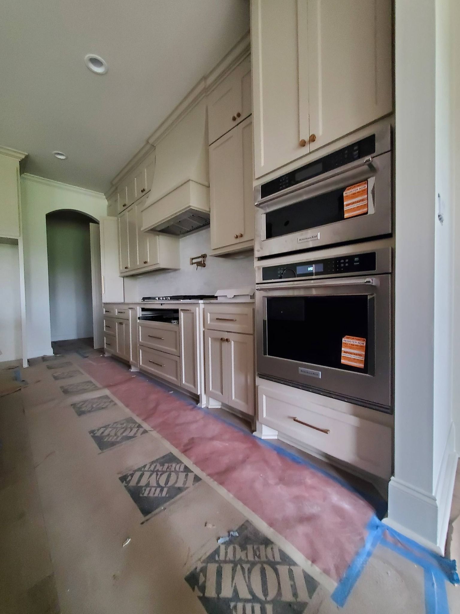 Narrow kitchen hallway with beige cabinets, built-in ovens, and a rug on the floor