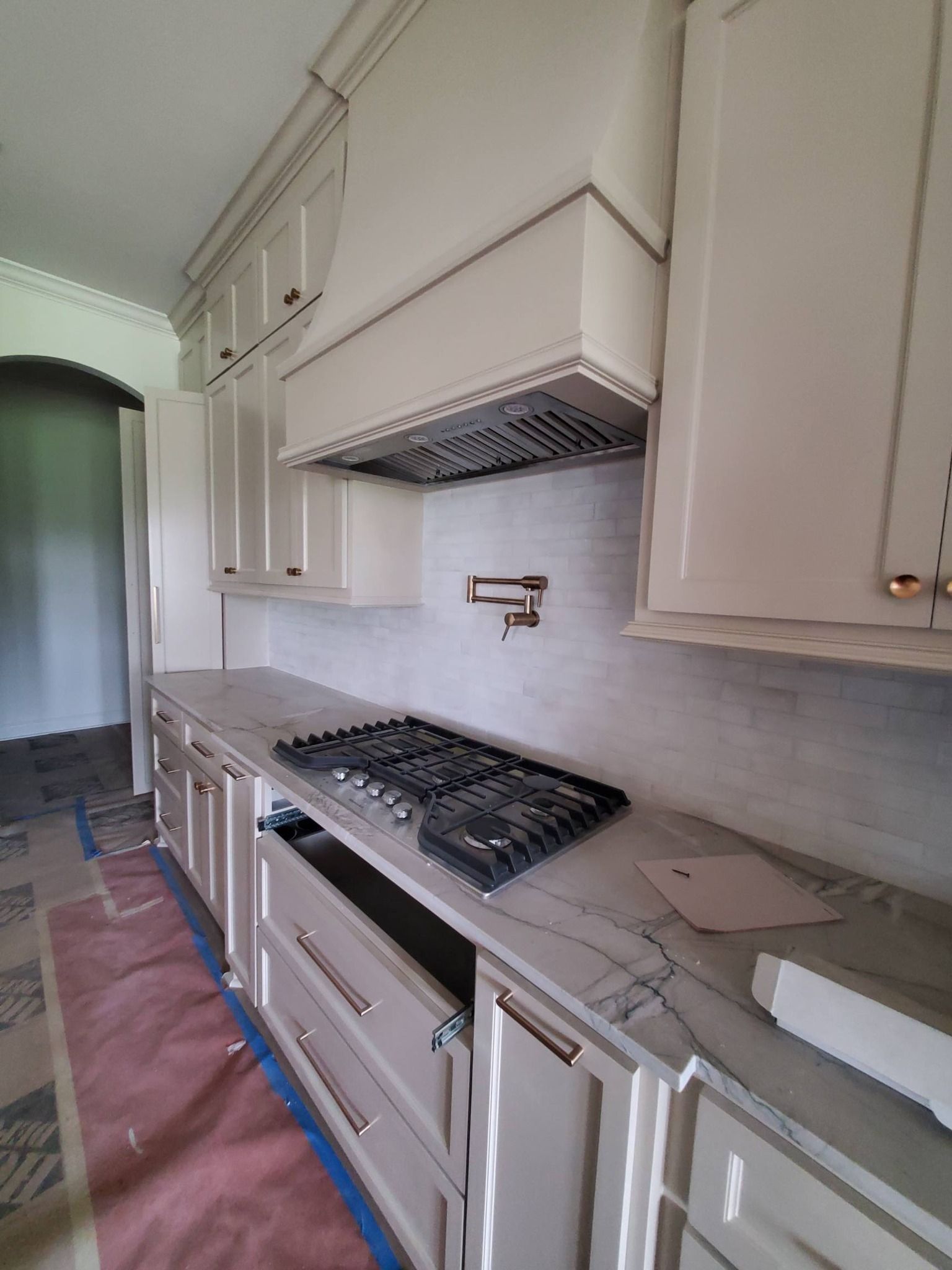Narrow galley kitchen with white cabinets, gas cooktop, hood, and light countertop.
