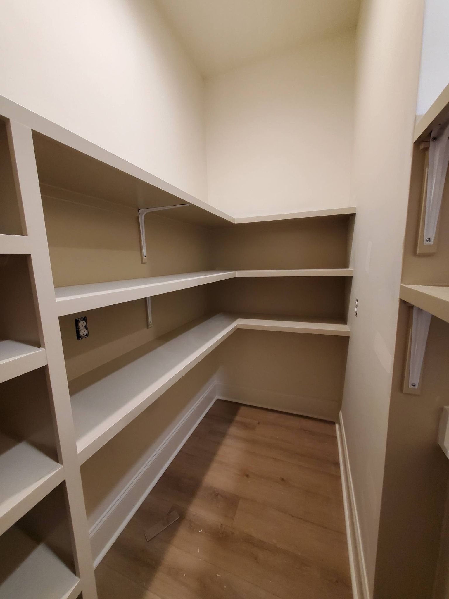 Empty walk-in closet with beige shelves and wood flooring.