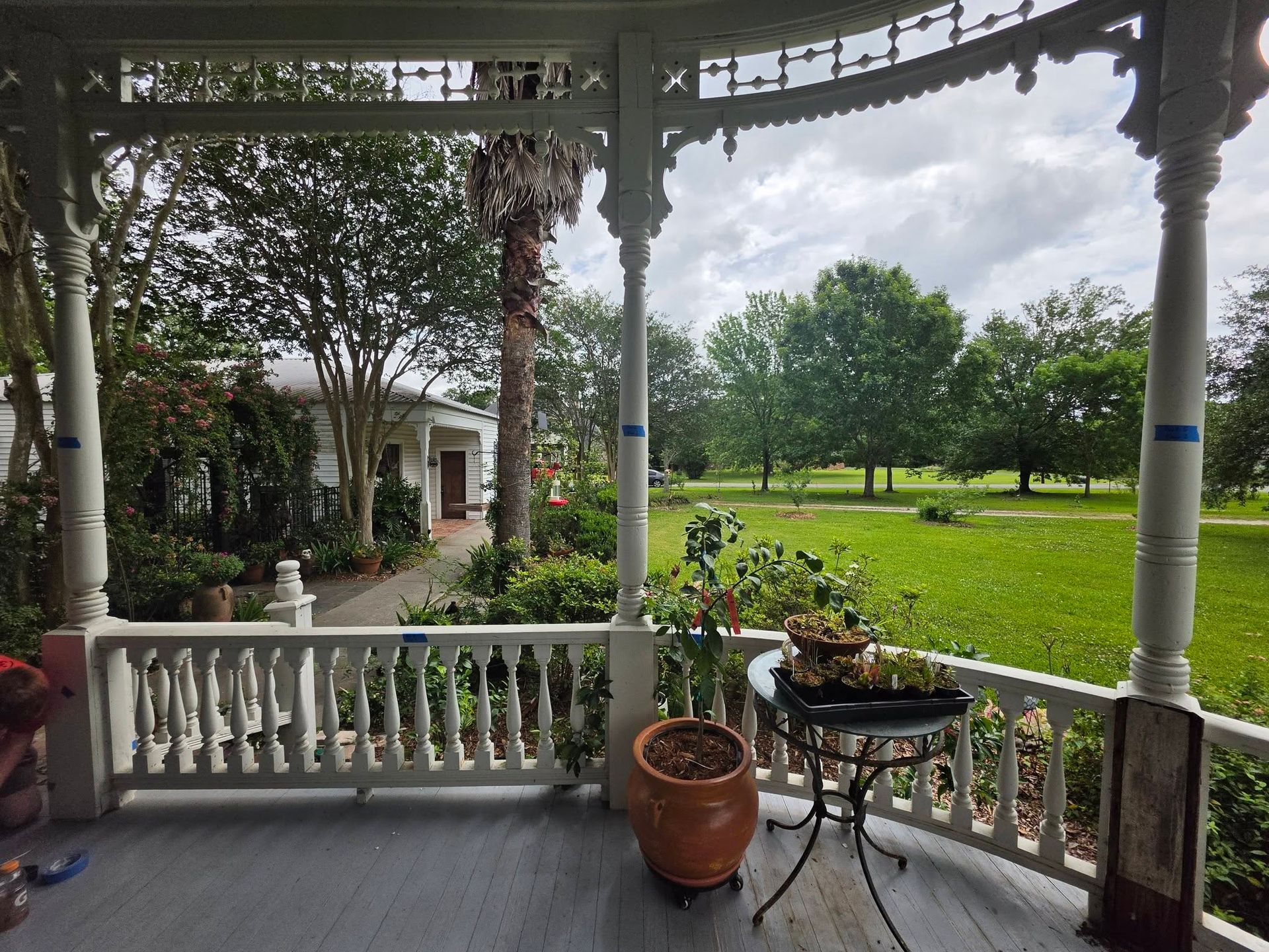Porch with white railing and potted plant overlooking a green lawn and trees