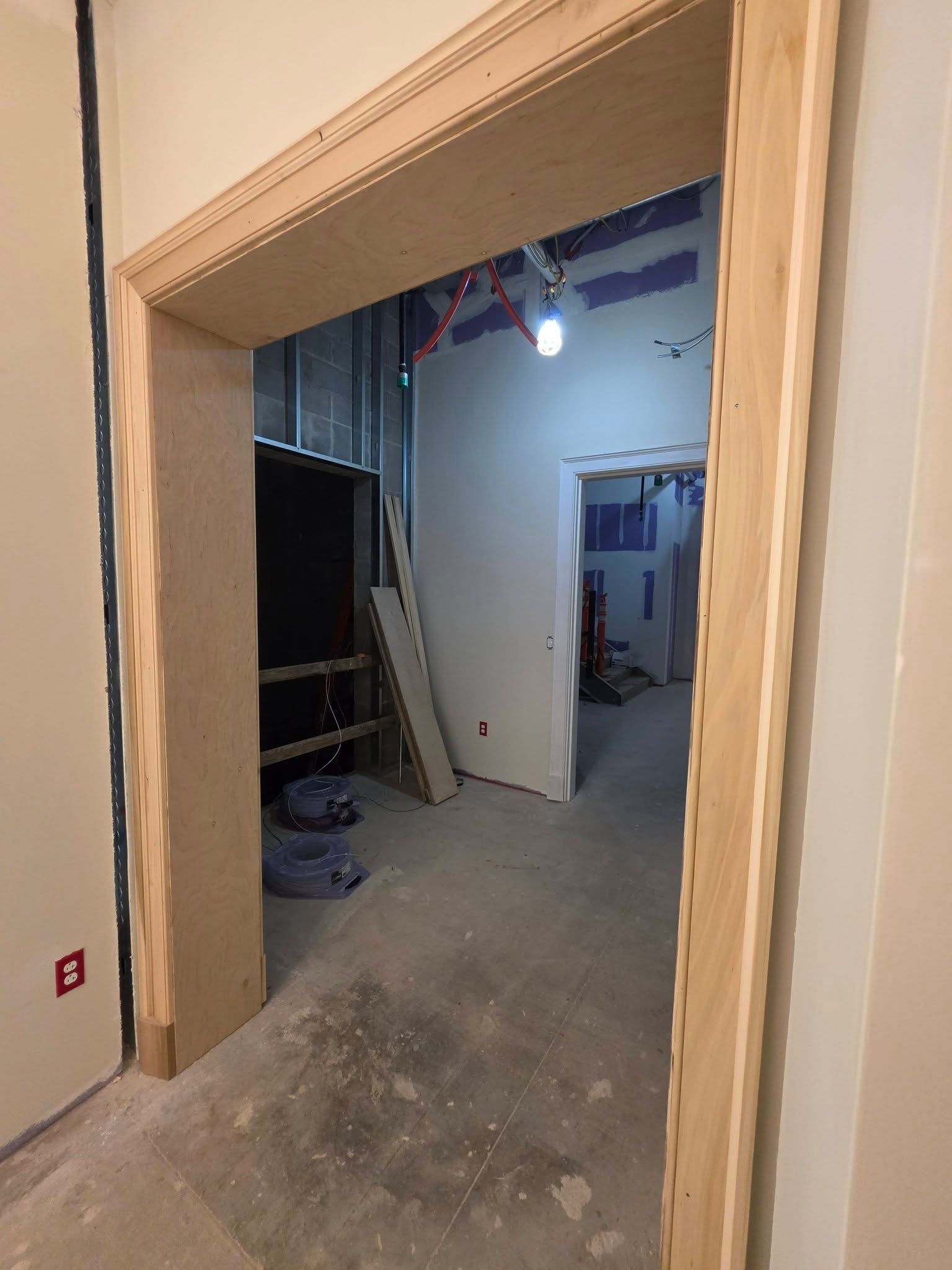 Unfinished interior doorway leading to a dusty hallway with exposed framing and construction materials