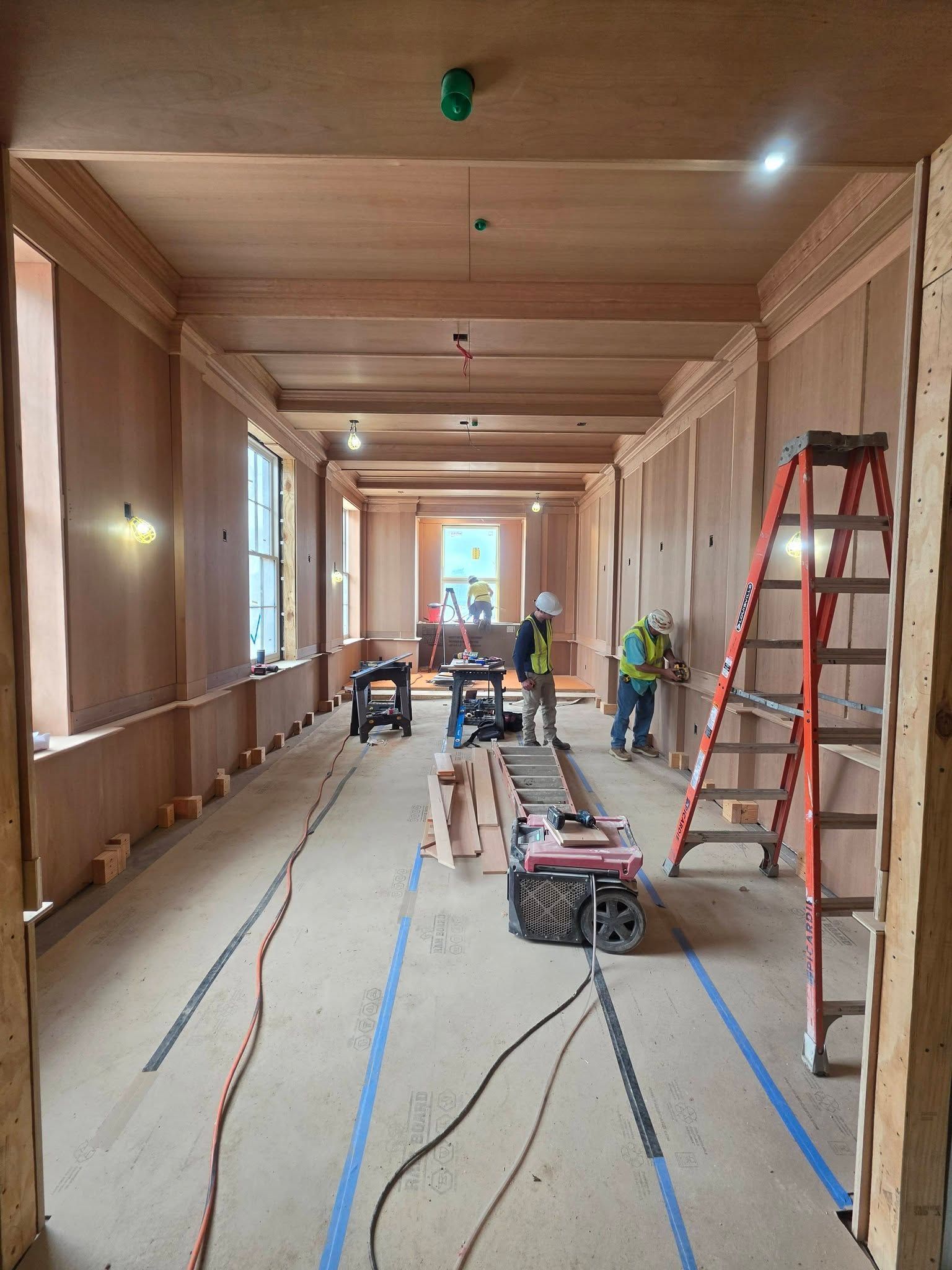 Long unfinished hallway with ladders, tools, and construction materials on the floor.