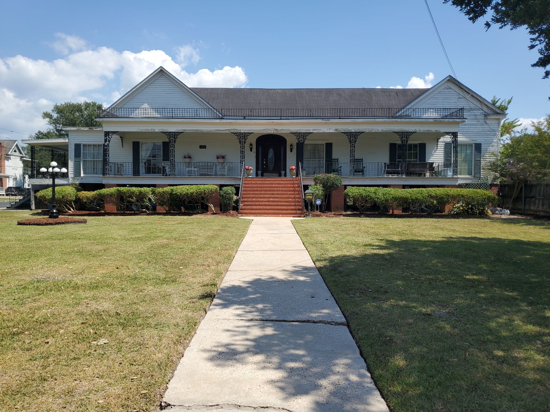 Front view of a white house with a porch, red steps, and a concrete walkway across a green lawn
