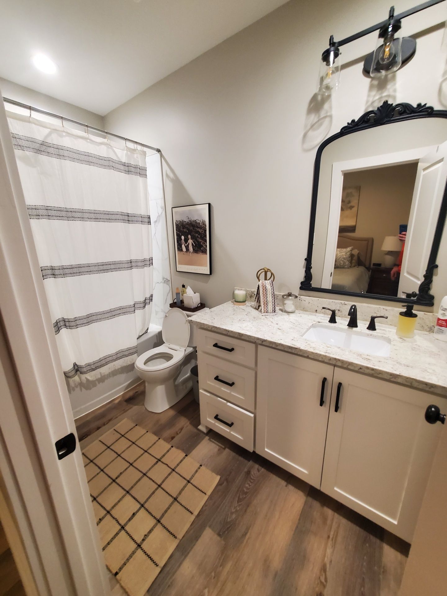 Bathroom with beige vanity, large mirror, white sink, toilet, shower curtain, and wood-look floor.