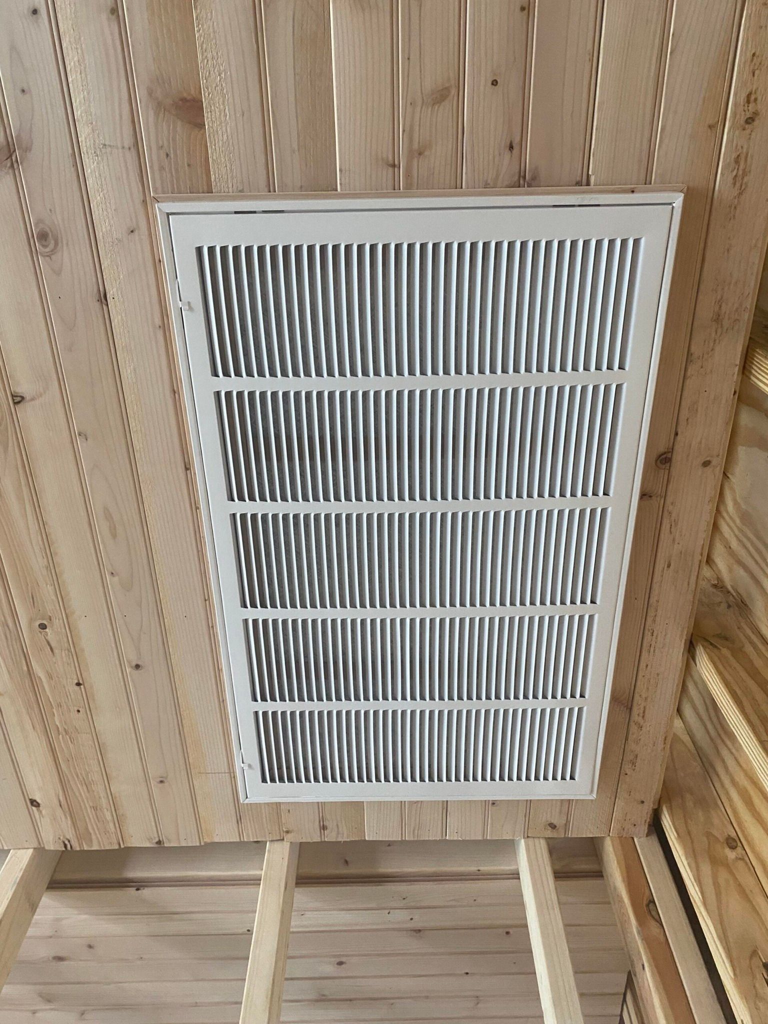 An air filter mounted within unfinished wooden ceiling joists.