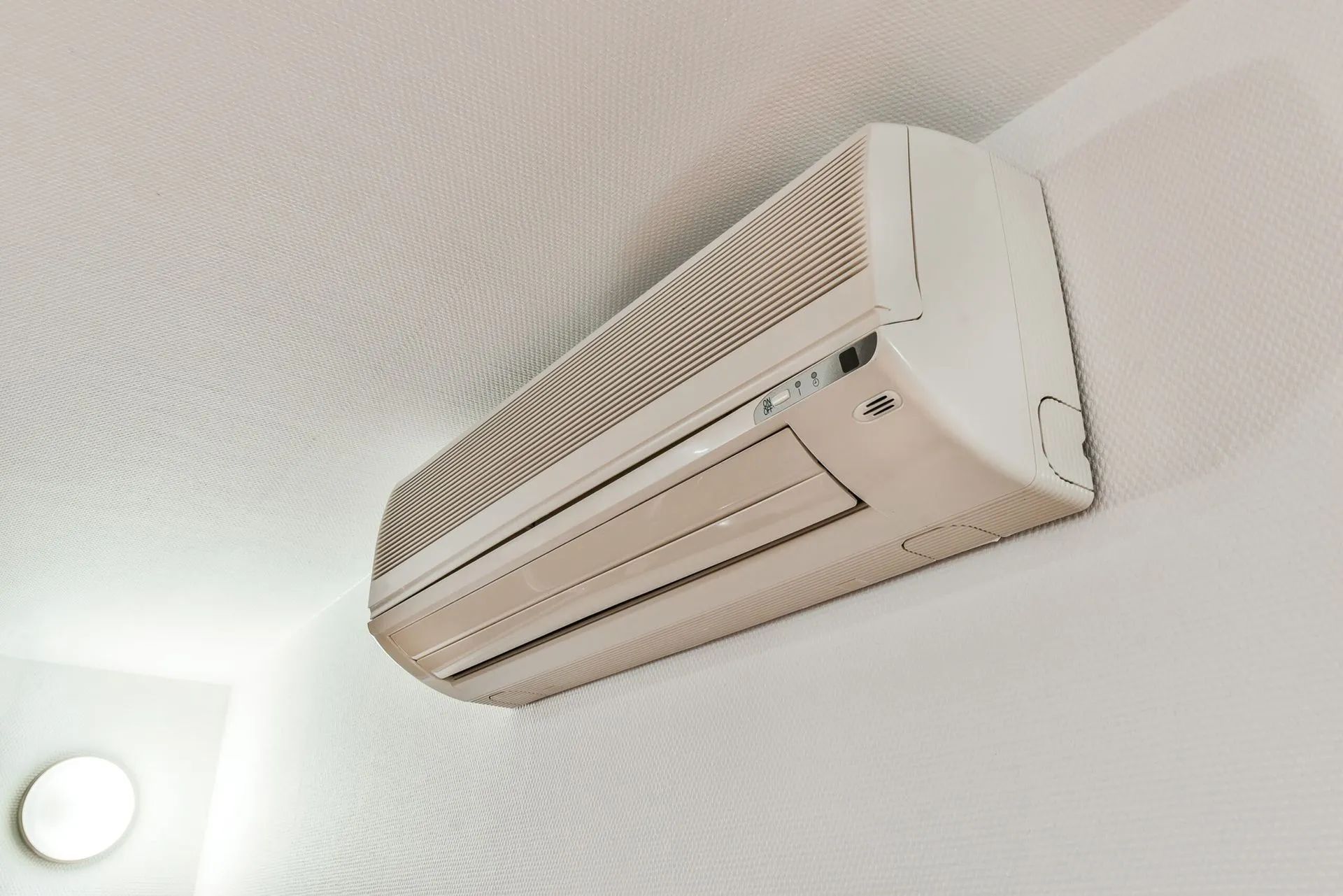 Wall-mounted white air conditioner on a ceiling, angled view indoors