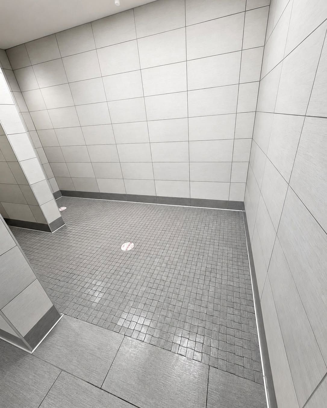 Empty tiled shower room with gray floor and white walls, viewed from the doorway.