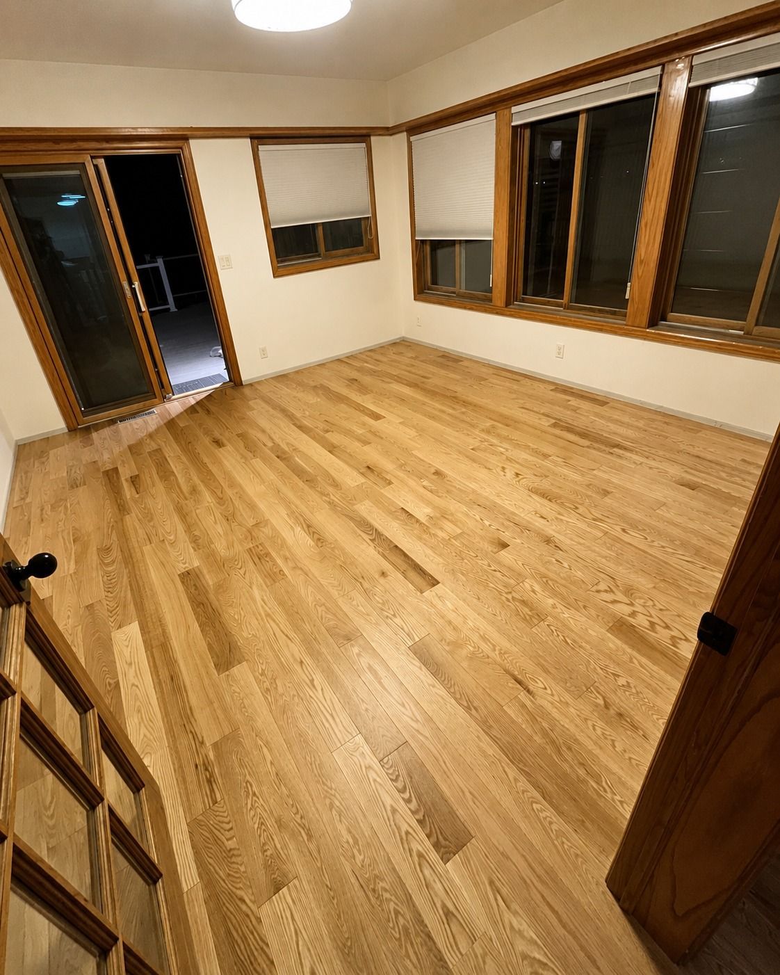 Empty wood-floored room with large windows and a doorway at left