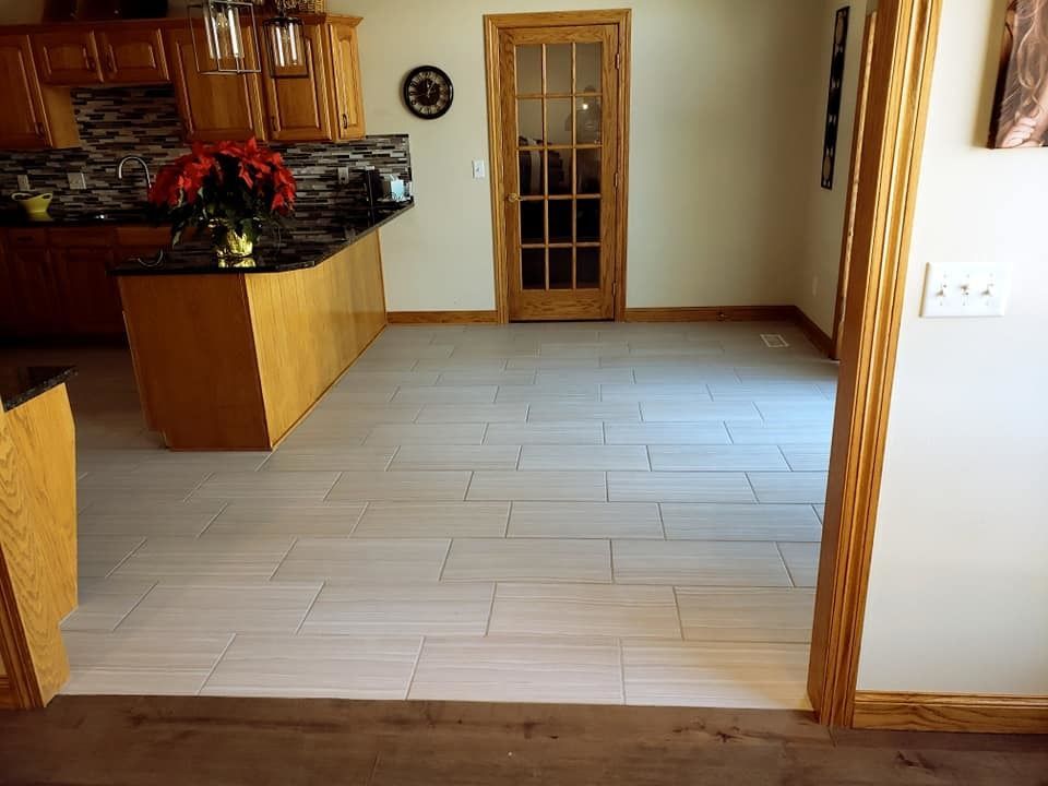 Empty kitchen and dining area with light tile flooring, wood trim, and a black granite counter with red flowers.