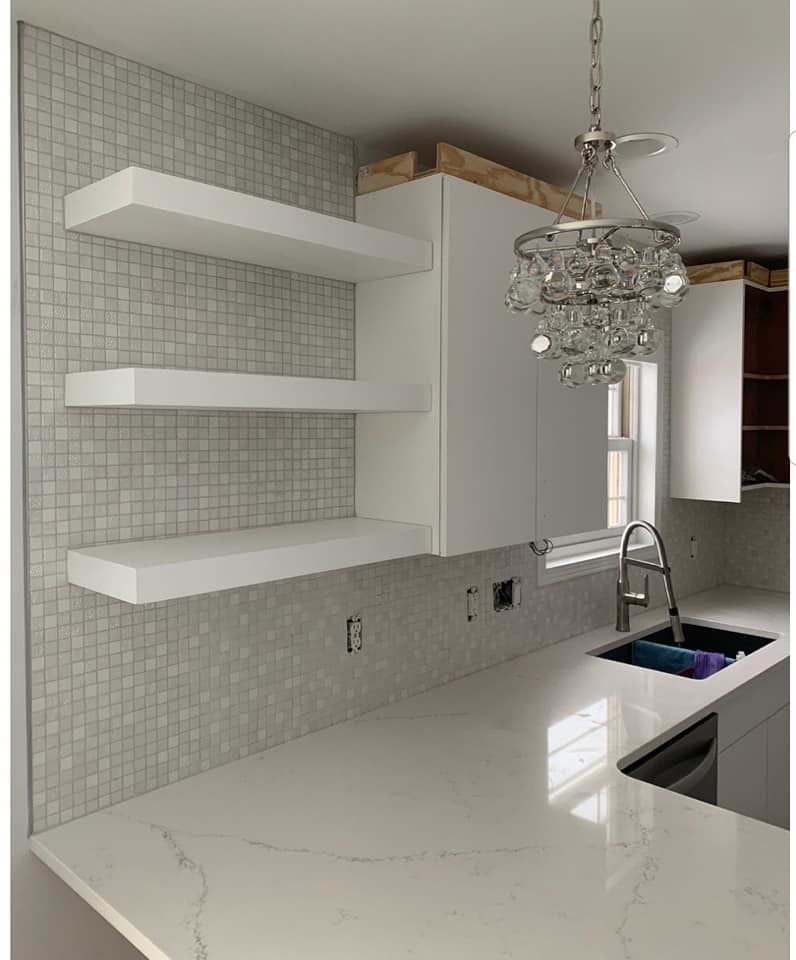 Modern white kitchen with marble island, floating shelves, mosaic backsplash, and crystal pendant light