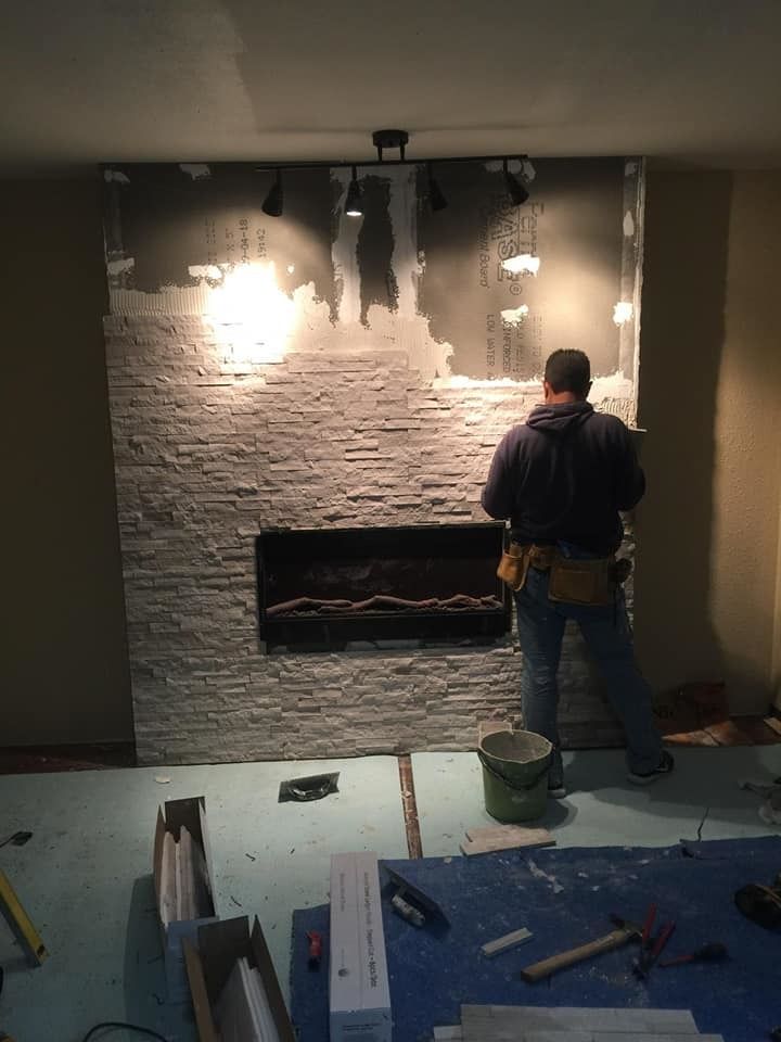 Worker painting a brick accent wall behind a recessed fireplace in a dim room