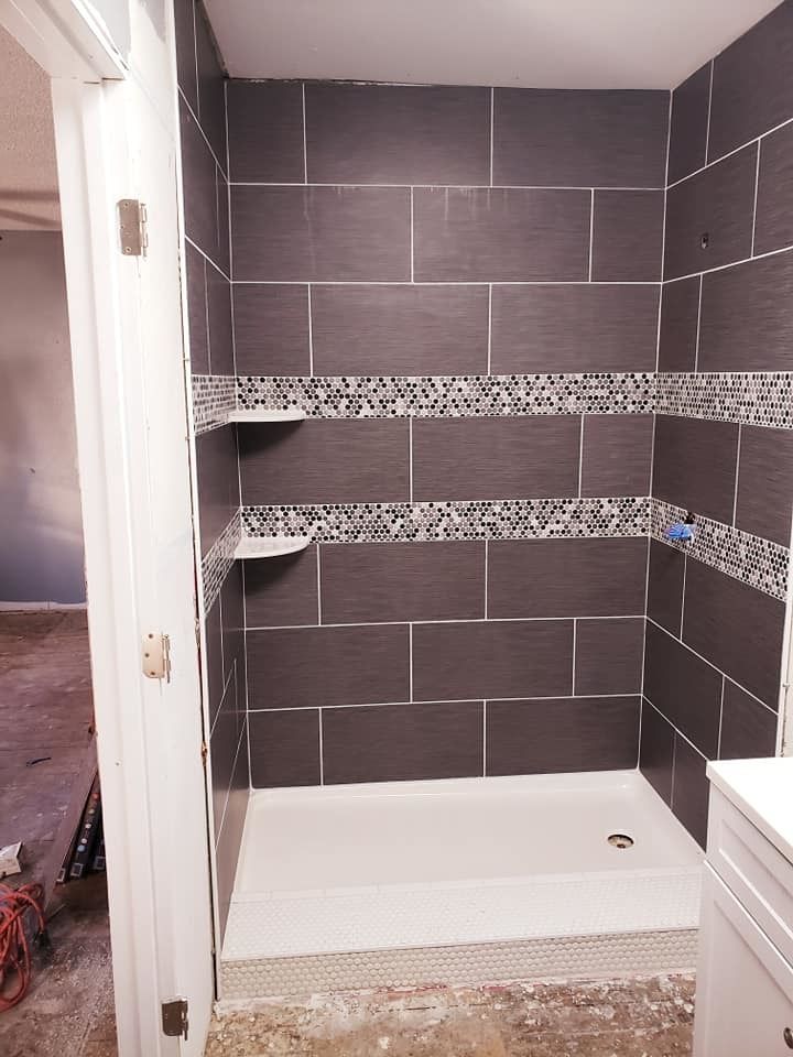 Tiled shower stall with dark gray walls, decorative shelf band, and white shower pan.